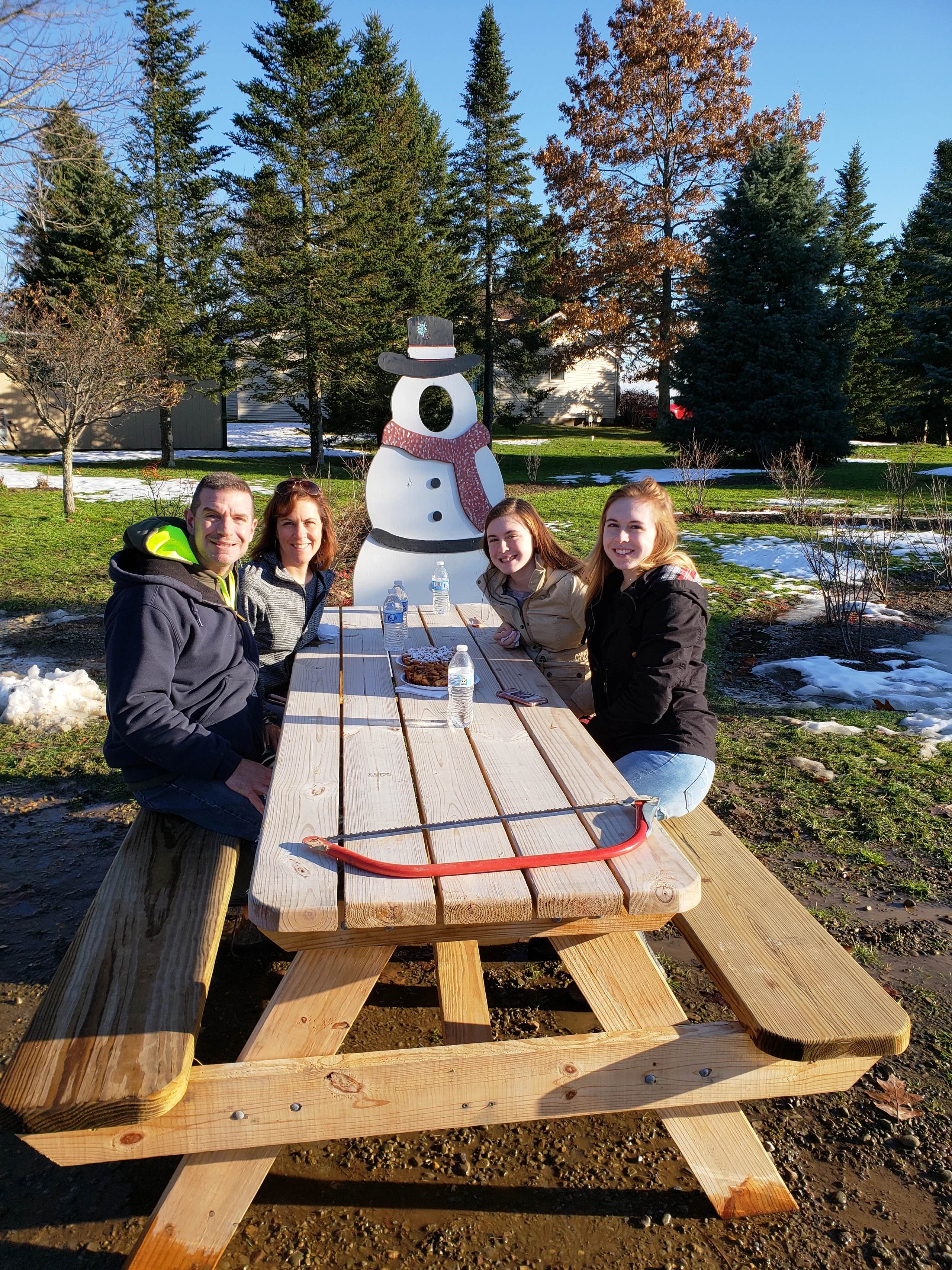 Four visitors at a picnic table beside a snowman display and evergreen trees at Country Pine Farm.