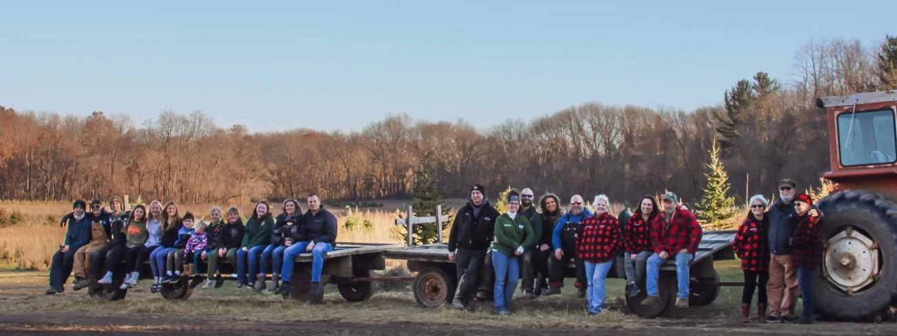 Visitors sitting and standing beside a tractor and field wagons at Broadview Christmas Tree Farm.