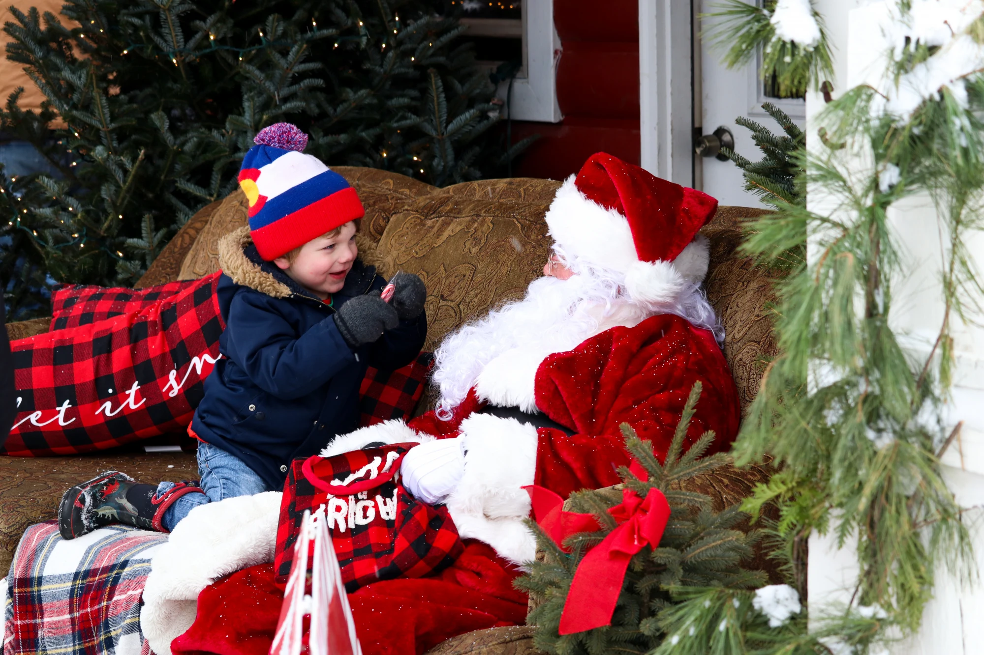 Santa sitting with a child on a couch among Christmas trees at Dutchman Tree Farms.
