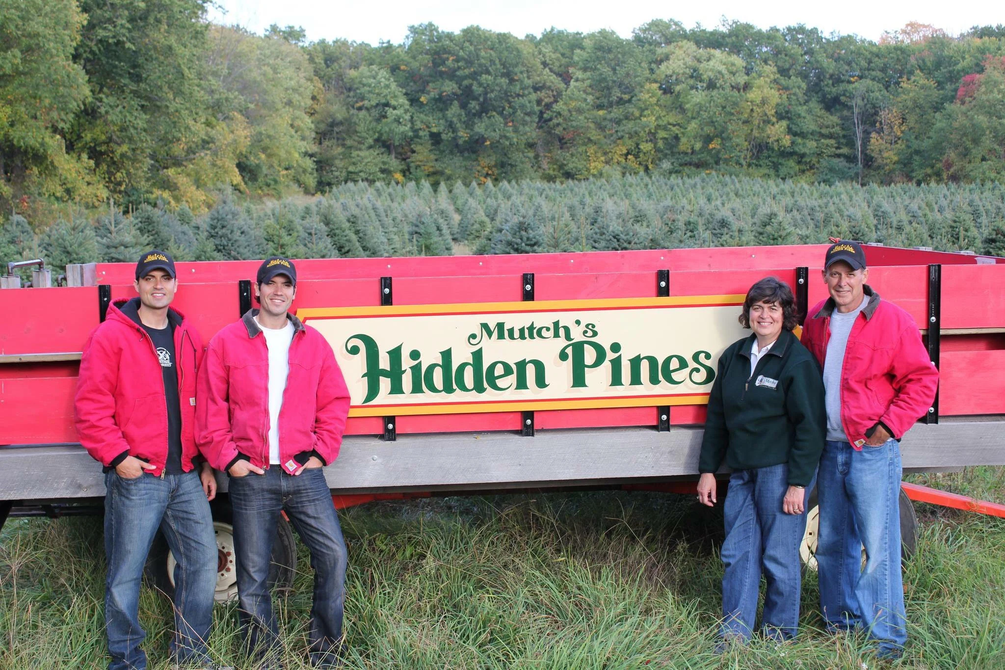 The Mutch family beside their red farm wagon and Christmas tree fields.