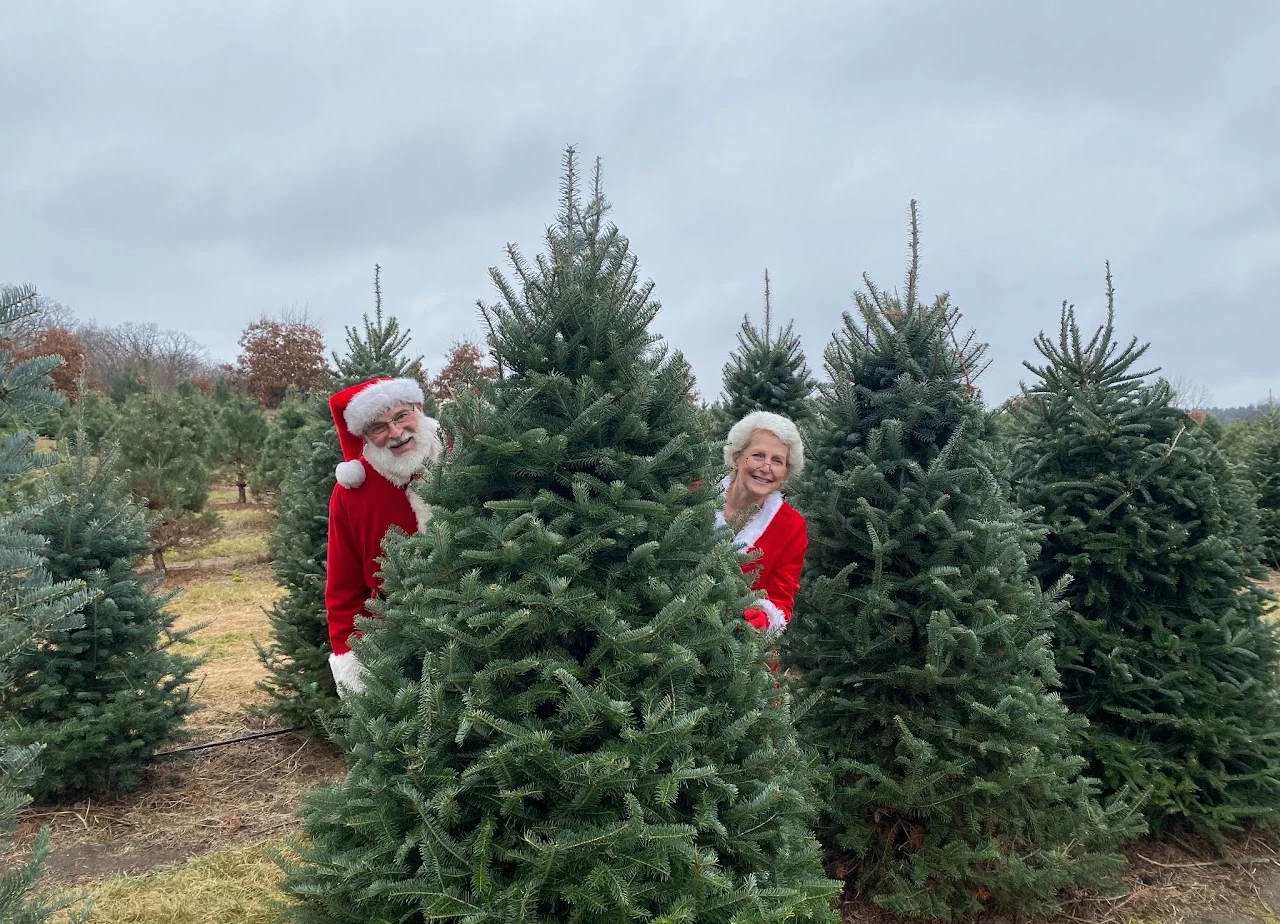 Santa and Mrs. Claus beside evergreen trees at Sinnissippi