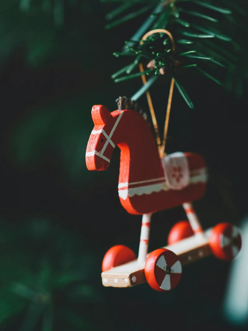 A red and white wooden rocking-horse ornament hangs from a loop on an evergreen branch.
