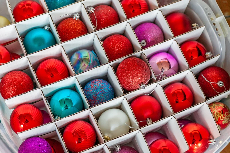 Red, blue, purple and silver Christmas baubles arranged in individual cardboard compartments inside a clear storage box.